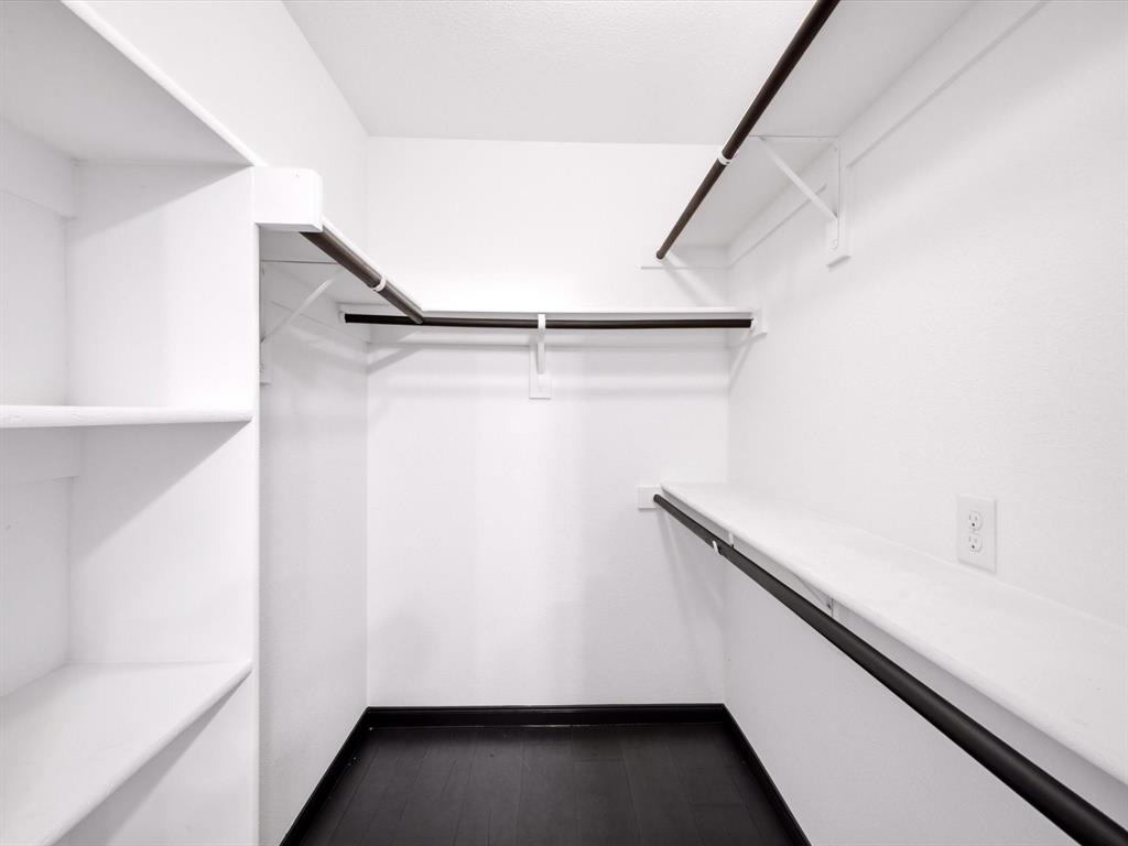 Walk-in closet featuring multi-level hanging rods, integrated wall shelving, and dark-finish flooring