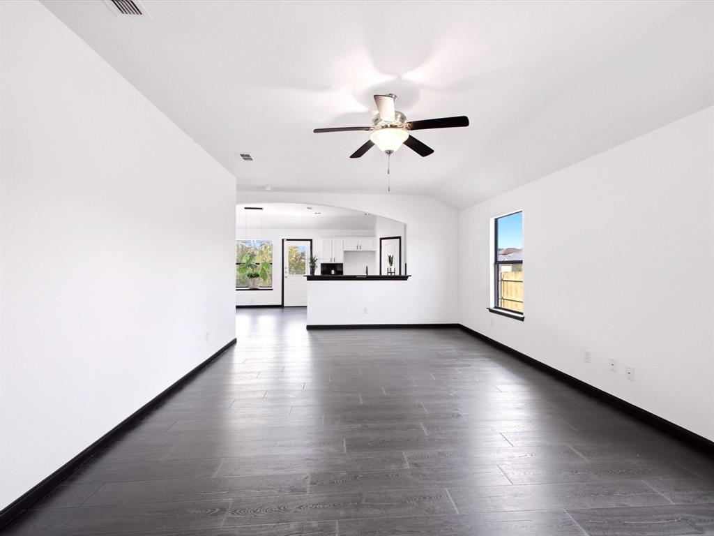 Interior space featuring dark wood-finish flooring, vaulted ceilings, a central ceiling fan with integrated lighting, and a pass-through opening