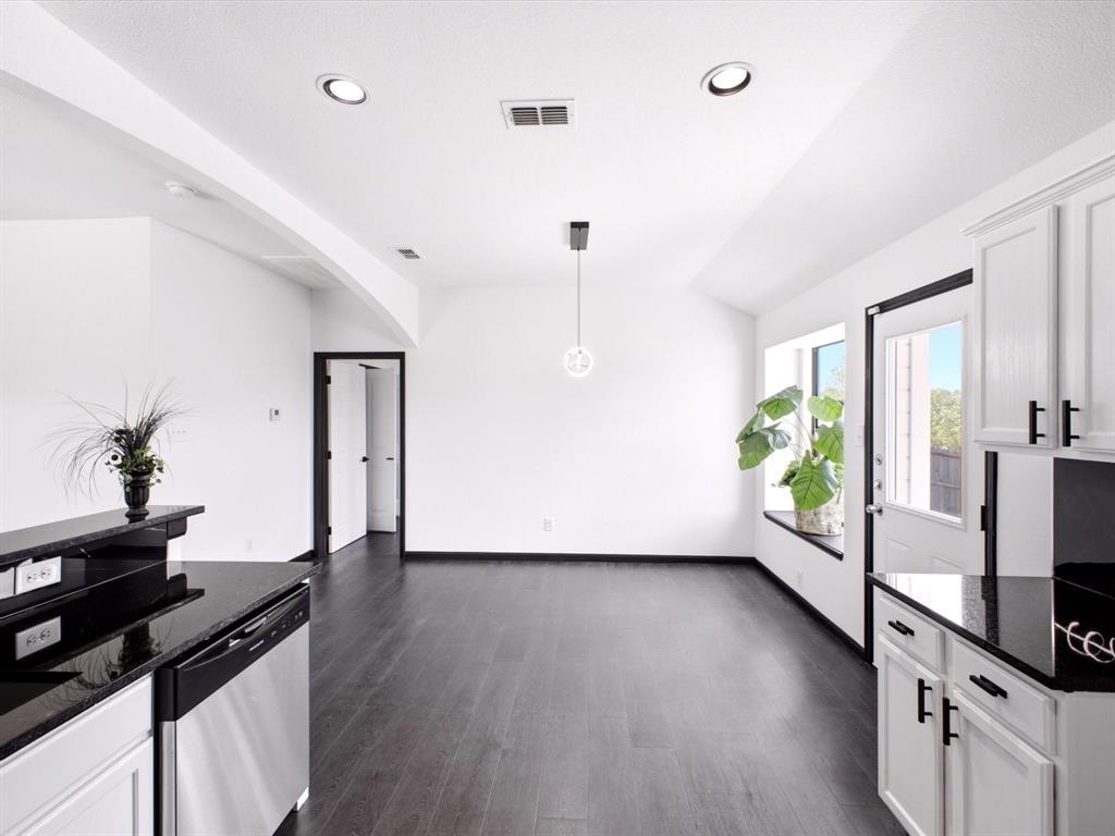 Kitchen featuring dark stone countertops, white cabinetry with matte black hardware, stainless steel dishwasher, wood-finish flooring, and a recessed window ledge