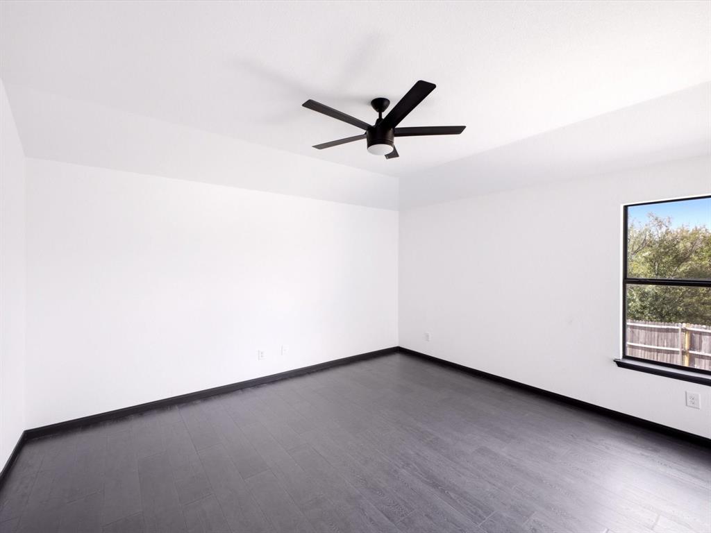 Neutral-toned interior featuring dark wood-finish flooring, white walls, and a matte black ceiling fan with integrated lighting