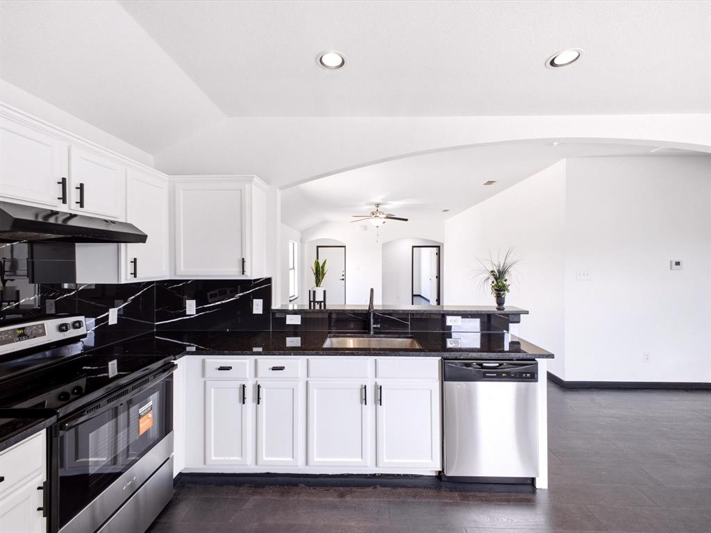Kitchen featuring white cabinetry with matte black hardware, high-contrast stone-finish backsplash, dark countertops, integrated stainless steel dishwasher, and recessed ceiling lighting