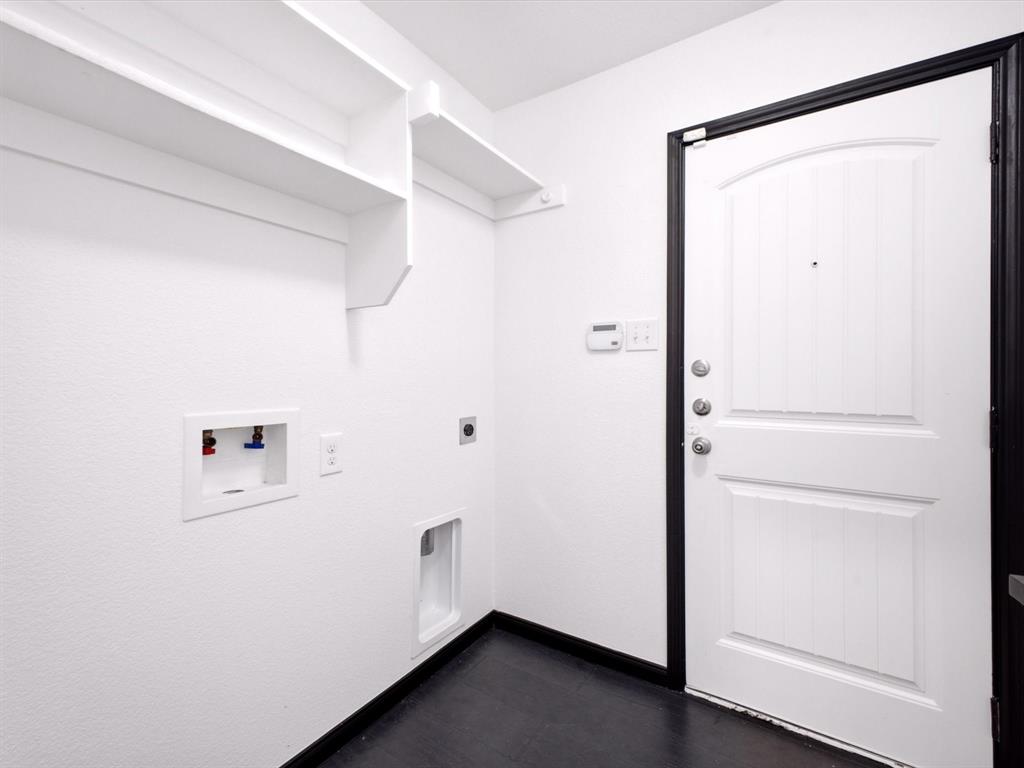 Utility area featuring white built-in wall shelving, dedicated water hookups, dark flooring, and a solid-core door with a high-contrast trim