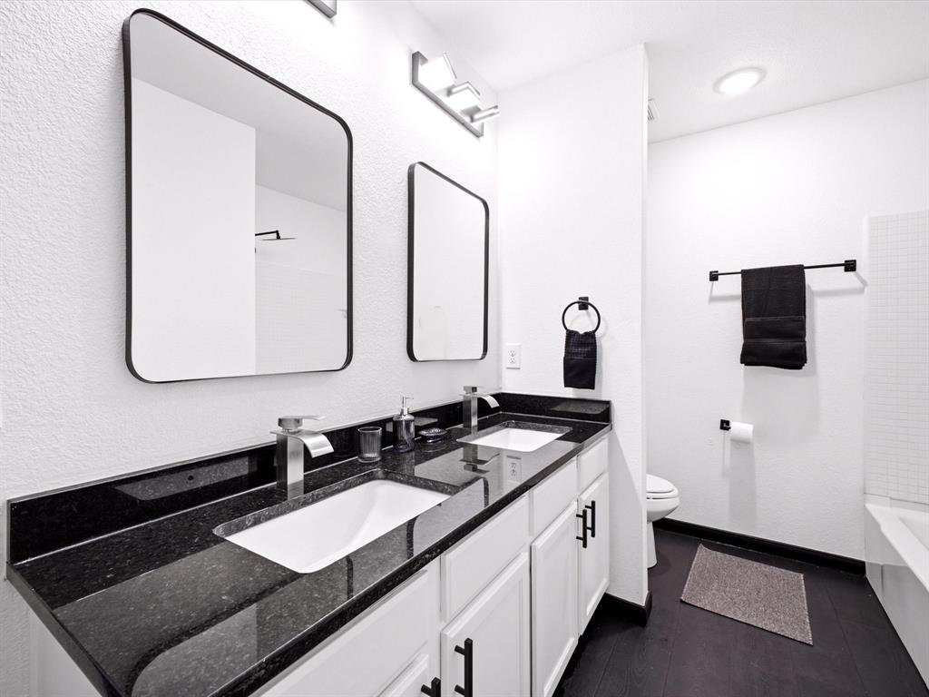 Dual-sink vanity with dark stone countertops, undermount rectangular basins, matte black hardware, and matching wall-mounted mirrors
