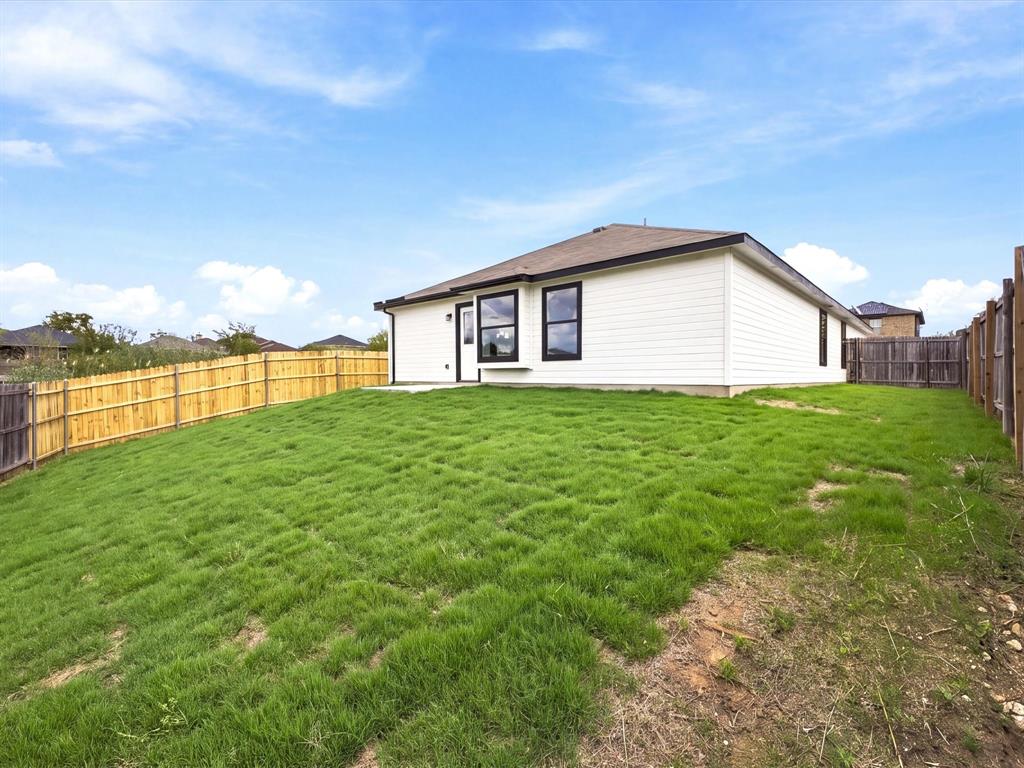 Exterior of the residence featuring horizontal white siding, dark window frames, a neutral-toned roof, and a fenced-in grassy yard
