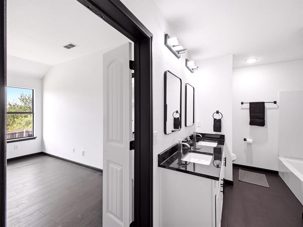 Dual-sink vanity with a dark stone countertop, undermount sinks, sleek rectangular mirrors, and dark-finished hardware