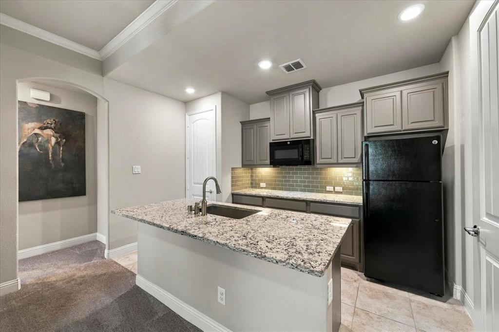 Suite Kitchenette features recessed lighting, gray cabinetry, a subway tile backsplash with under-cabinet lighting, a built-in microwave, and a center island with countertops. Ceramic tile flooring extends throughout, transitioning to carpet in the sitting room and hall.