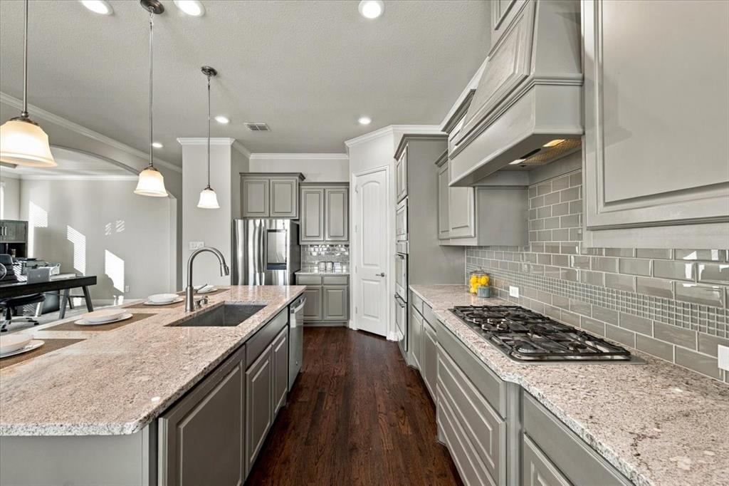 Kitchen features recessed lighting, a subway tile backsplash with a mosaic accent band, a gas cooktop, an island with an undermount sink and stainless dishwasher, a pantry, and an arched opening to the office. Wood flooring extends throughout. Kitchen features recessed lighting, a subway tile backsplash with a mosaic accent band, a gas cooktop, an island with an undermount sink and stainless dishwasher, a pantry, and an arched opening to the office. Wood flooring extends throughout.