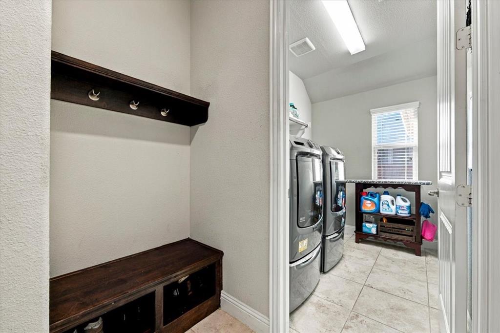 Laundry Room features an angled ceiling section, an overhead light fixture, a wall-mounted shelf, a window, and a built-in drop zone outside the entry with a wall-mounted hook rail and a bench with storage cubbies. Ceramic tile flooring extends throughout.