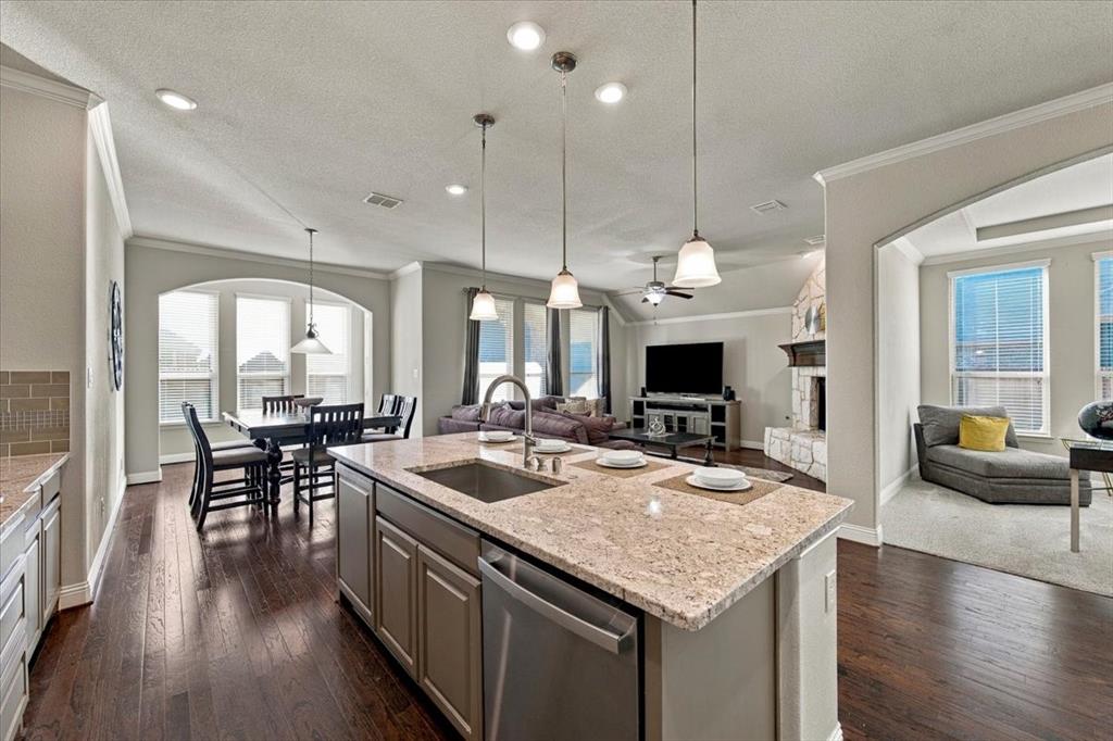 Kitchen features a center island with an undermount sink overlooking the living room, an arched opening to the office, and an open layout to the dining area. Wood flooring extends throughout, transitioning to carpet in the office.