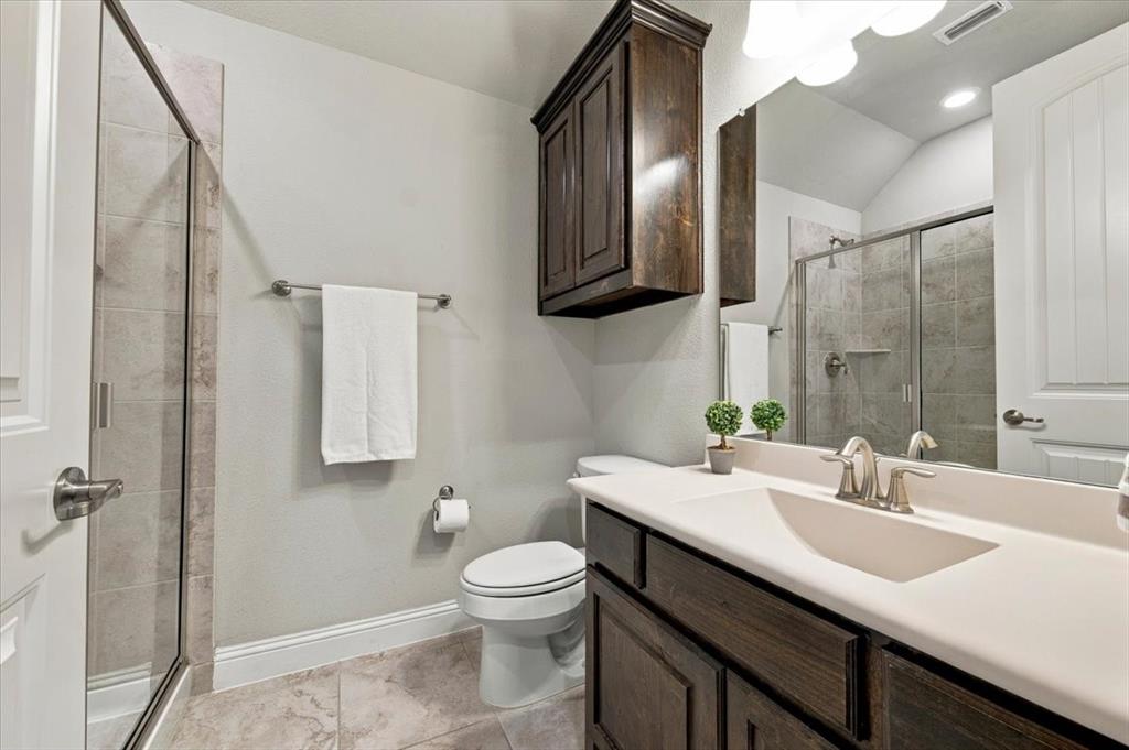 Suite Bathroom features a vanity light fixture, a cabinet above the toilet, a single vanity with countertop and cabinet storage, and a walk-in shower with a glass door and tile surround. Ceramic tile flooring extends throughout.