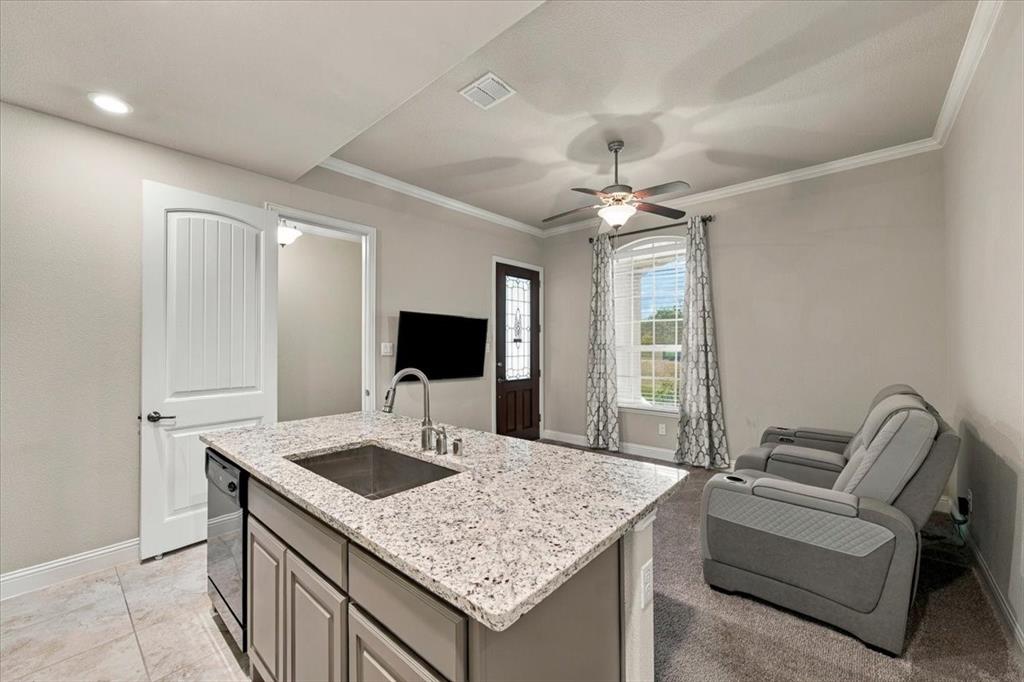 Suite Kitchenette features an island with an undermount sink, built-in dishwasher, and cabinet storage, with an open layout to the sitting room. Ceramic tile flooring extends throughout, transitioning to carpet in the sitting room.