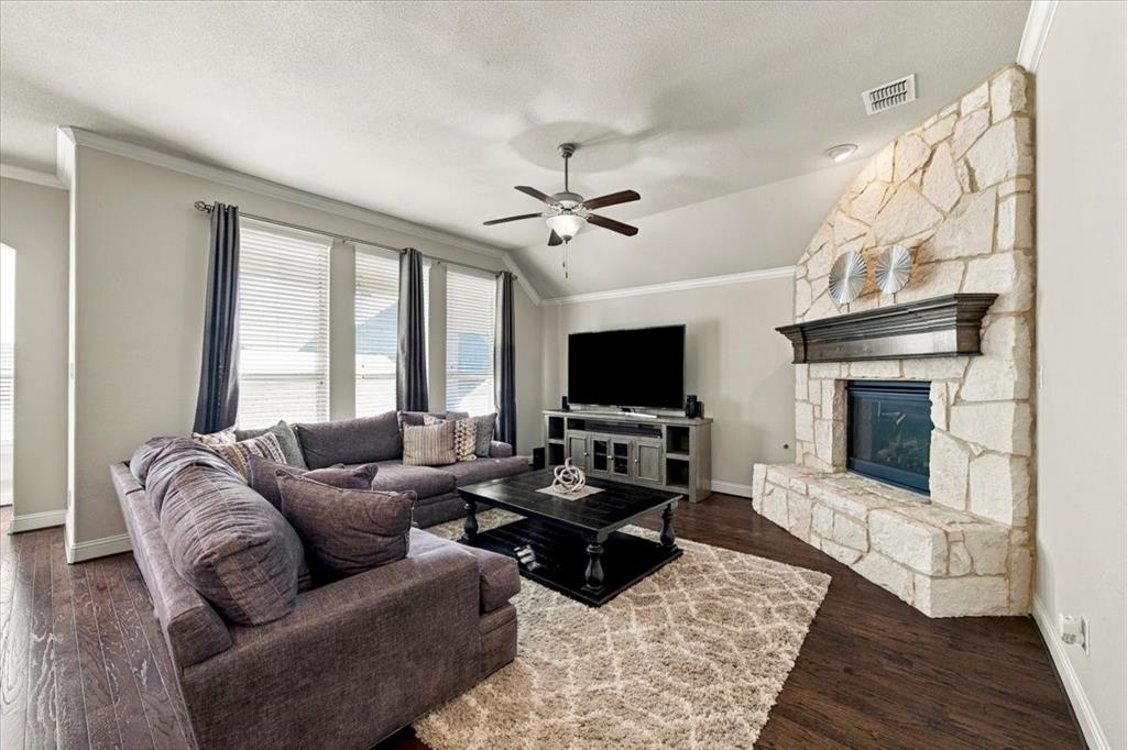 Living Room features an angled ceiling section, a gas log fireplace with gas starter, floor-to-ceiling stonework and a raised stone hearth, and a row of three windows. Wood flooring extends throughout. Living Room features an angled ceiling section, a gas log fireplace with gas starter, floor-to-ceiling stonework and a raised stone hearth, and a row of three windows. Wood flooring extends throughout.