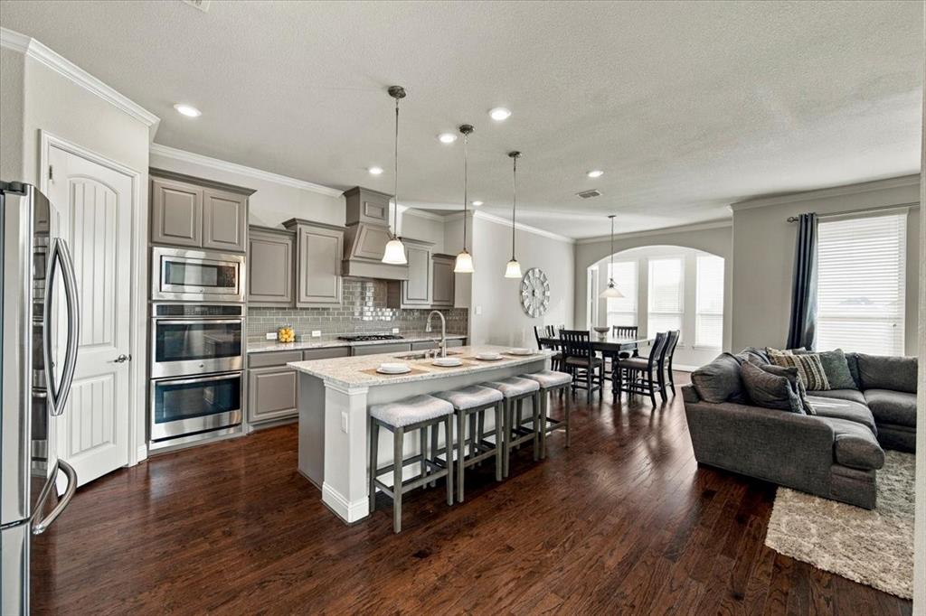 Kitchen features recessed lighting that continues into the dining area, island seating, and an open layout connecting the kitchen, dining area, and living room. Wood flooring extends throughout.
