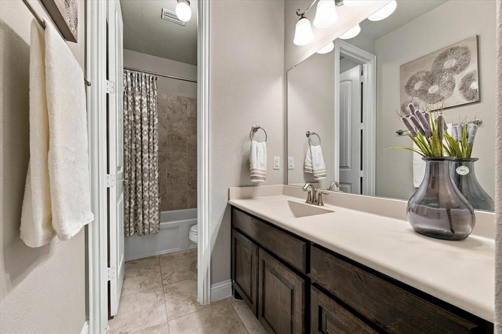 Secondary Bathroom features a vanity light fixture, a vanity with countertop and cabinet storage, and a separate compartment with a door, toilet, and tub/shower combination. Ceramic tile flooring extends throughout.