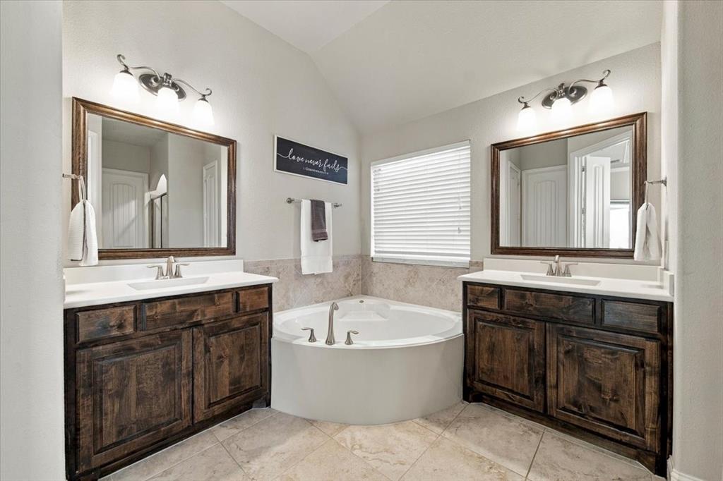 Primary Bathroom features dual sinks with countertops and cabinet storage at each vanity, positioned on either side of the garden tub. Ceramic tile flooring extends throughout.