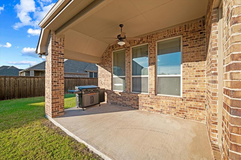 Covered Patio features a ceiling fan with light fixture, brick columns and walls, three windows, and a view of the fenced backyard. Concrete flooring extends throughout.