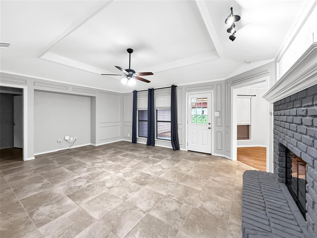 Tray ceiling with molding, tile flooring, painted brick fireplace, and built-in wall paneling