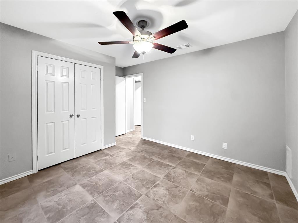 Neutral-toned wall finish, large-format tile flooring, double-door closet, and integrated ceiling fan with light fixture