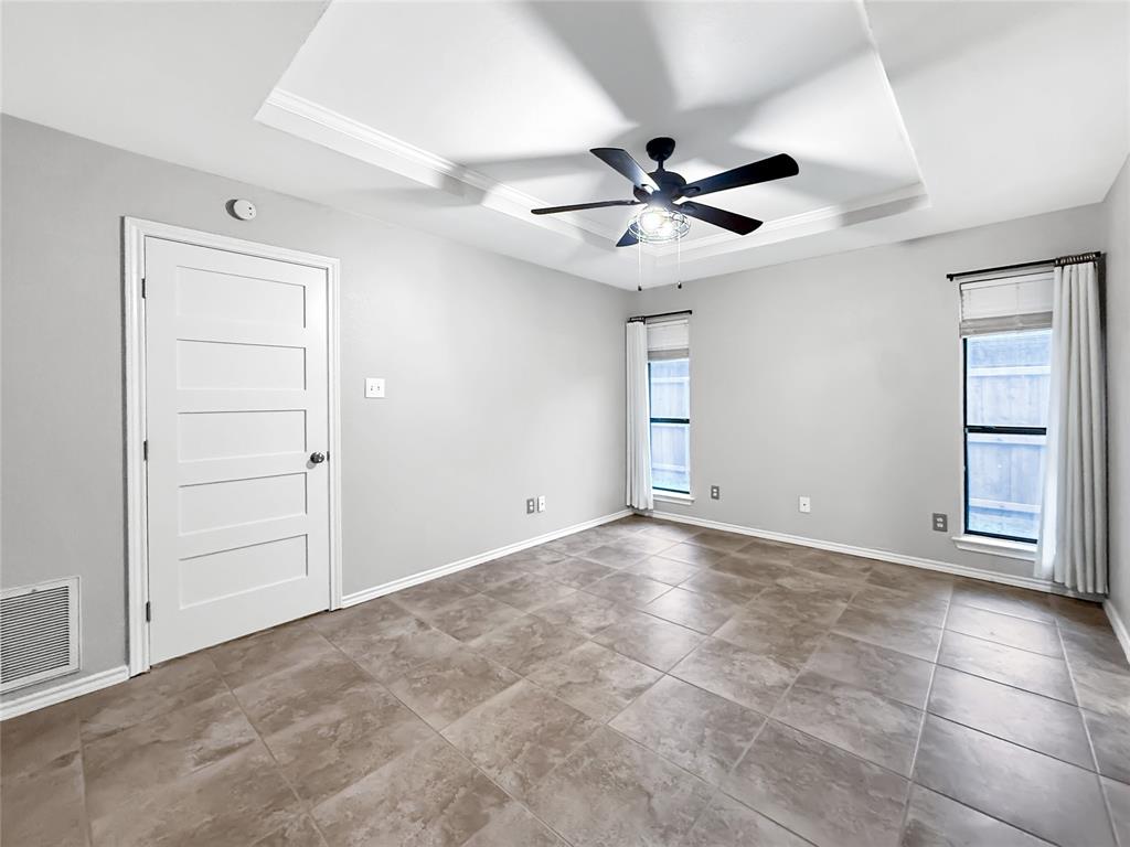 Tray ceiling with a central multi-blade ceiling fan, neutral tile flooring, and a solid-core four-panel interior door