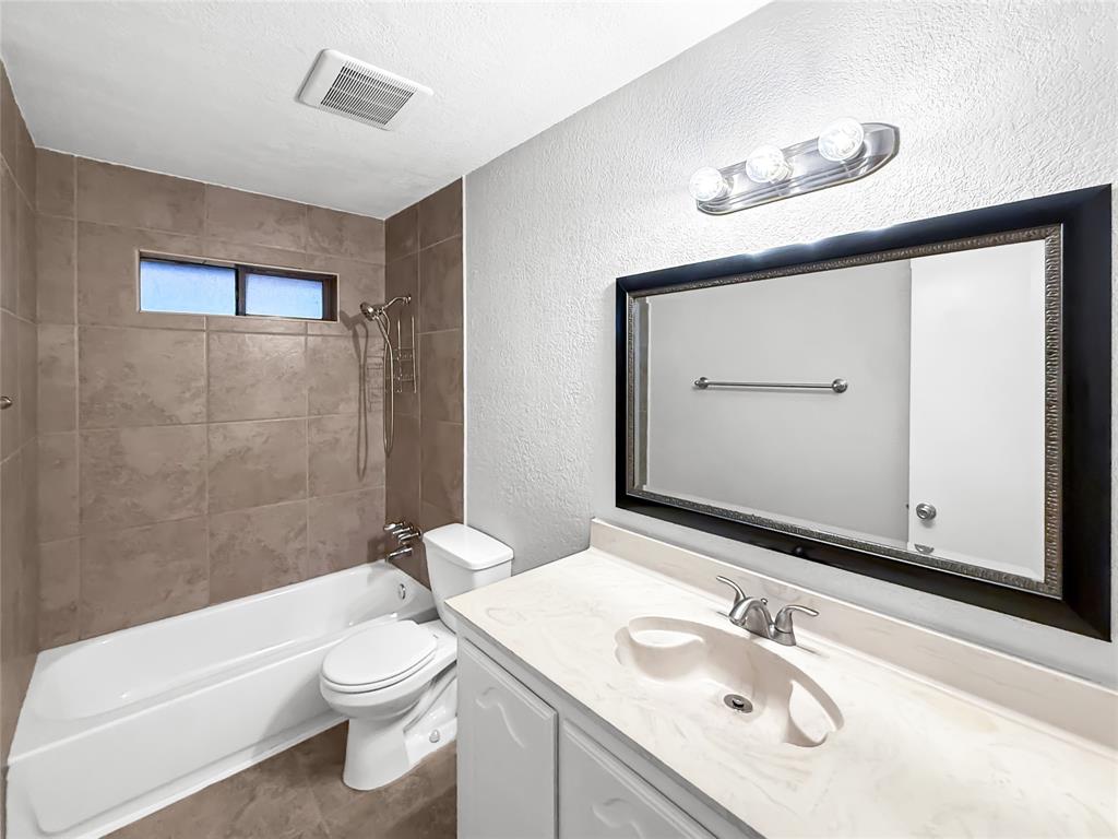 Bathroom featuring a vanity with a molded countertop, wall-mounted light fixture, framed mirror, and a tiled shower surround with a handheld shower head