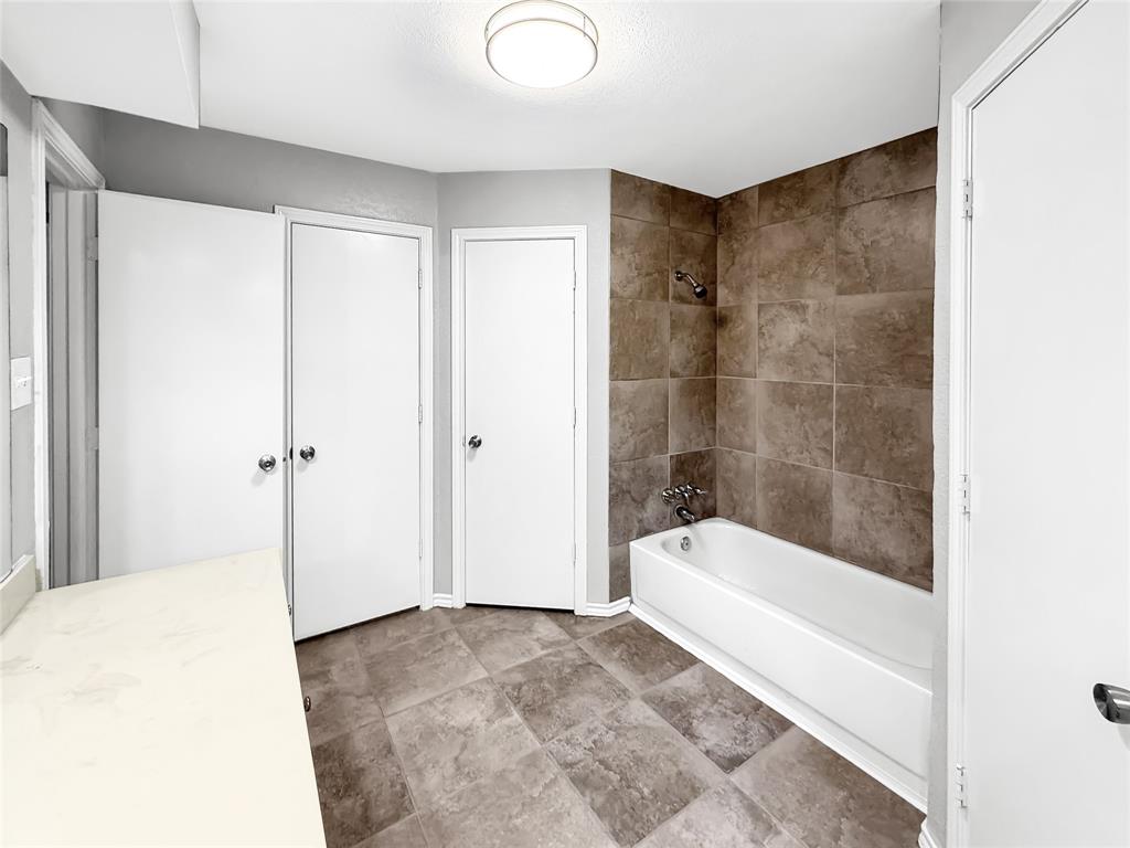 Bathroom featuring large-format ceramic floor tile, a deep-set bathtub, full-height wall tiling, a neutral vanity countertop, and a recessed ceiling light fixture