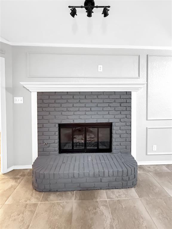 Fireplace featuring a grey-painted brick surround and raised hearth, capped with a white crown molding mantel, complemented by decorative wall molding and triple-track matte black ceiling lighting