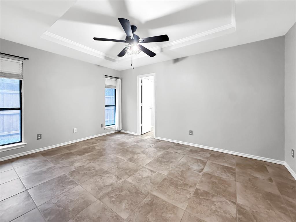 Interior room featuring a tray ceiling, ceiling fan with integrated lighting, tile flooring, and windows with neutral roller shades