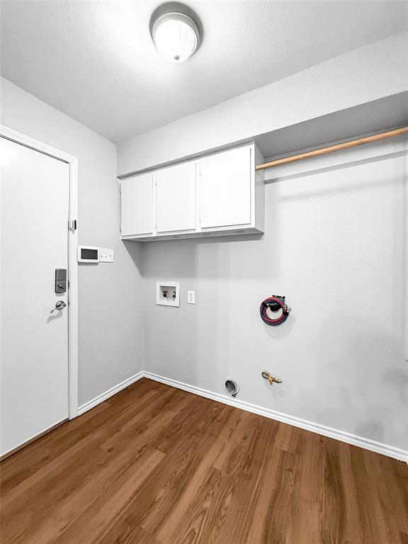 Utility space featuring wood-finish flooring, white wall-mounted cabinetry, a built-in hanging rod, dedicated water hookups, and a flush-mount ceiling light fixture