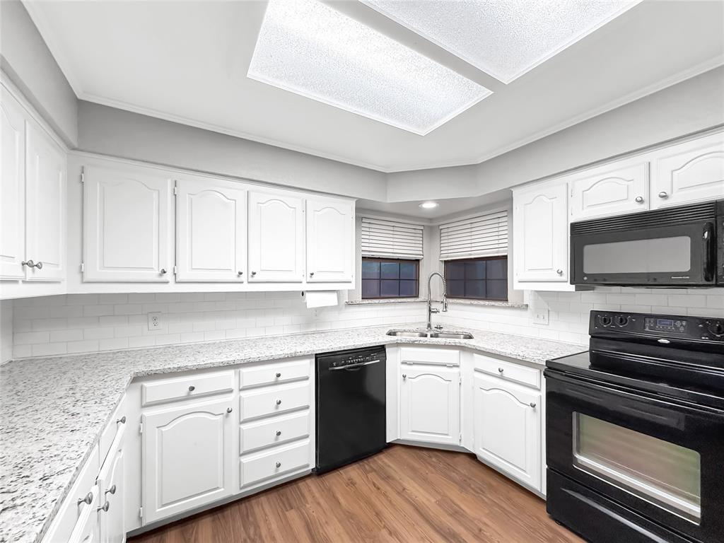 Kitchen featuring white cabinetry, light-toned stone-finish countertops, subway tile backsplash, wood-finish flooring, and black appliances