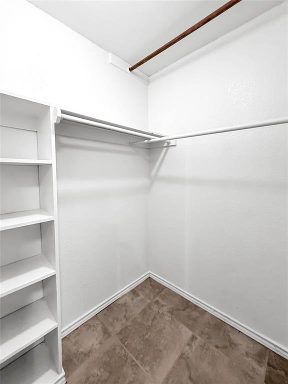 Storage space featuring built-in white shelving, integrated hanging rods, and tile flooring