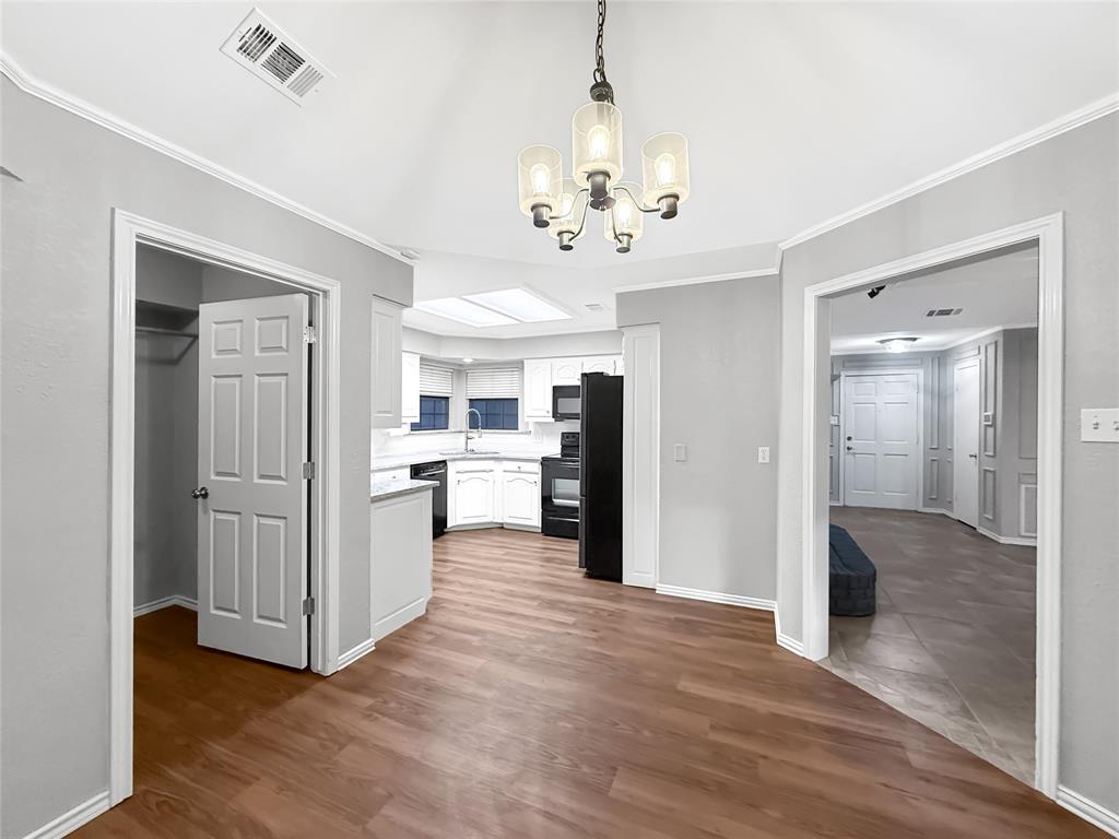Vaulted ceiling with a multi-light chandelier, wood-finish flooring, kitchen featuring built-in cabinetry and a skylight, and multi-panel interior doors