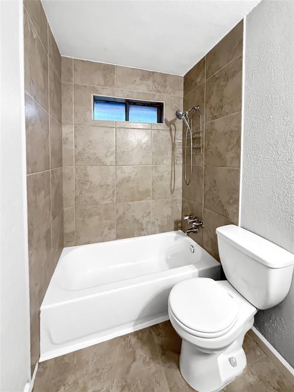 Full-size bathtub with surrounding large-format neutral-tone tile, handheld showerhead, and a horizontal privacy window
