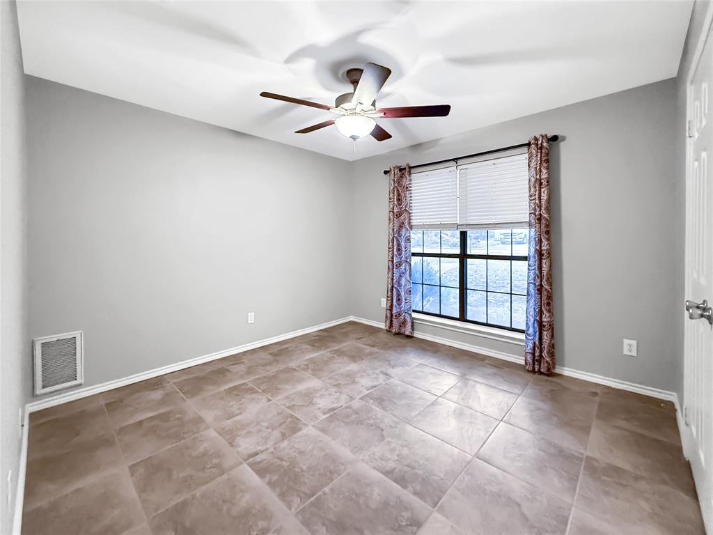 Room featuring large-format ceramic floor tile, neutral wall paint, a multi-blade ceiling fan with integrated lighting, and a single-pane window with a grid pattern