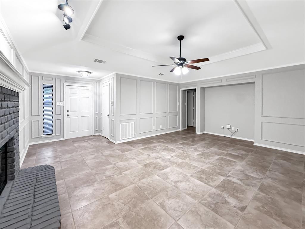Tray ceiling with recessed lighting, full-wall decorative wainscoting, large-format tile flooring, brick-surround fireplace, and central ceiling fan with integrated light fixture