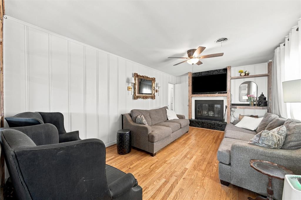Living area featuring wood-finish flooring, vertical paneling, and a fireplace with stone-style surround and integrated shelving
