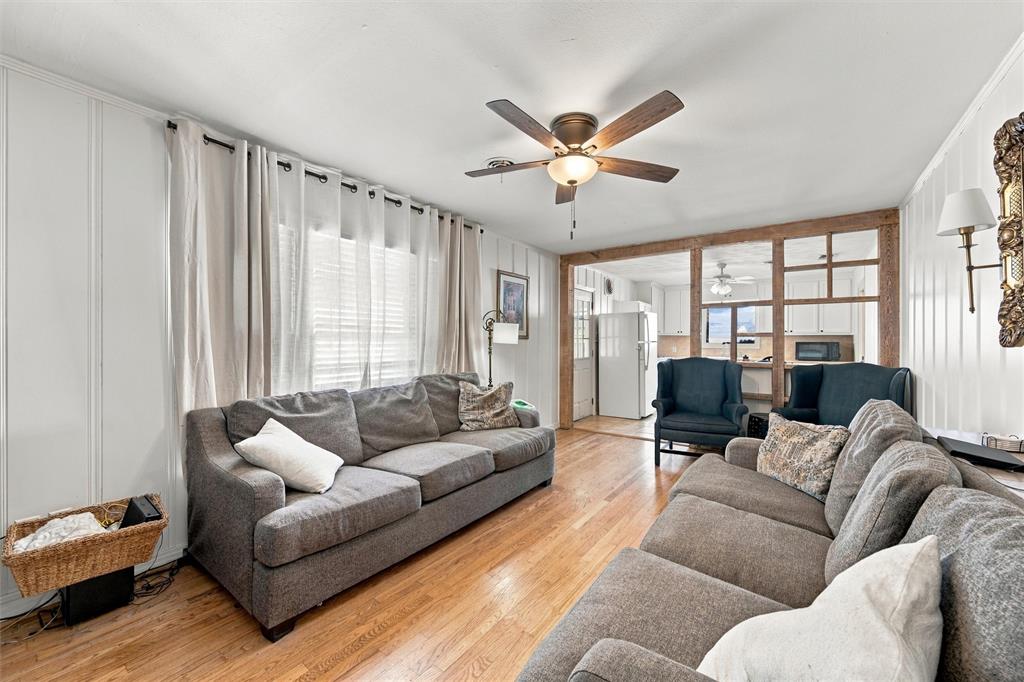 Living area featuring wood-finish flooring, vertical wall paneling, a ceiling fan with integrated light fixture, and a decorative open-frame wooden partition