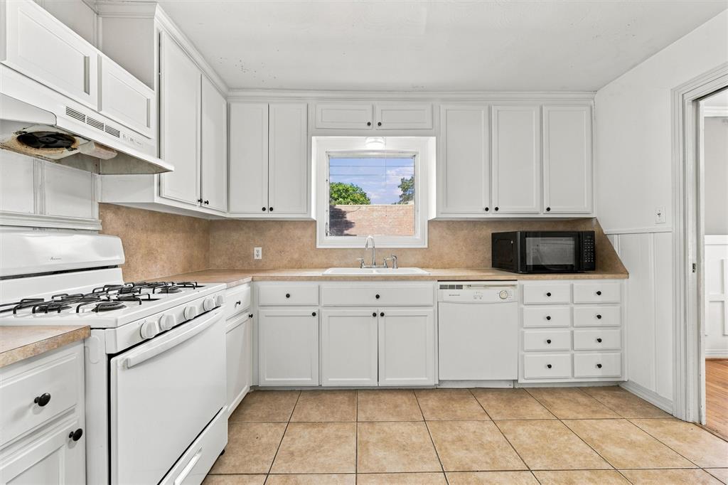 Kitchen featuring white cabinetry, neutral-toned tile backsplash, integrated gas range, neutral tile flooring, and a window over the sink