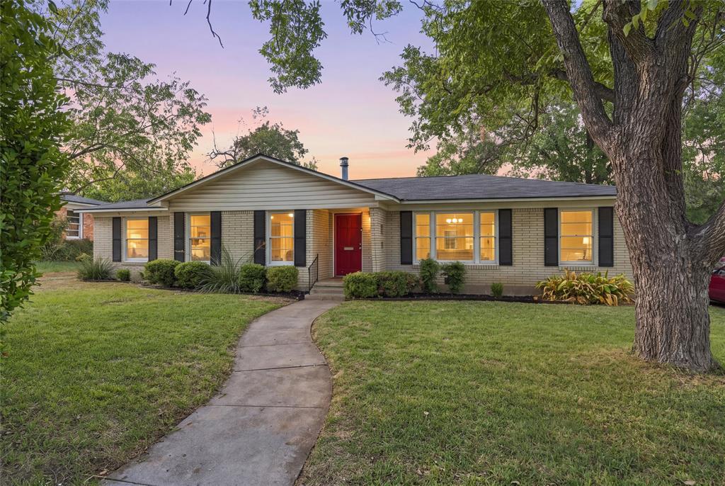 Ranch-style exterior featuring light-colored brick masonry, contrasting window shutters, a prominent red front door, and a concrete walkway