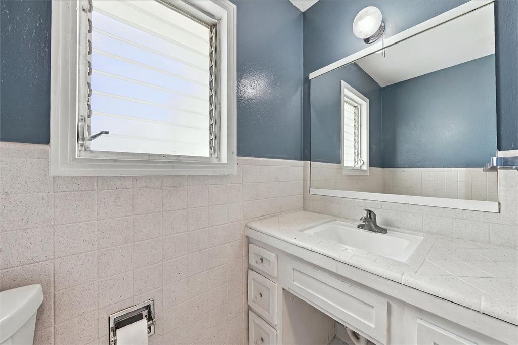 White vanity featuring an integrated sink, tile countertop, large wall-mounted mirror, louvered window, and chrome finish faucet