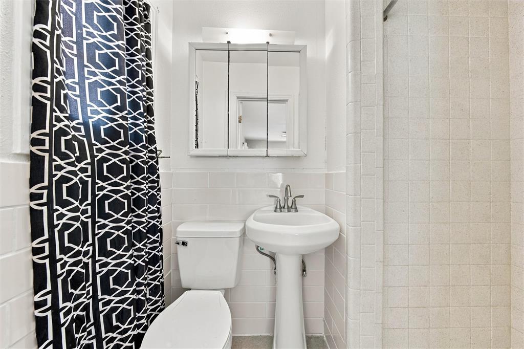 White pedestal sink with chrome faucet, tripartite mirrored medicine cabinet, and wall-tiled shower surround