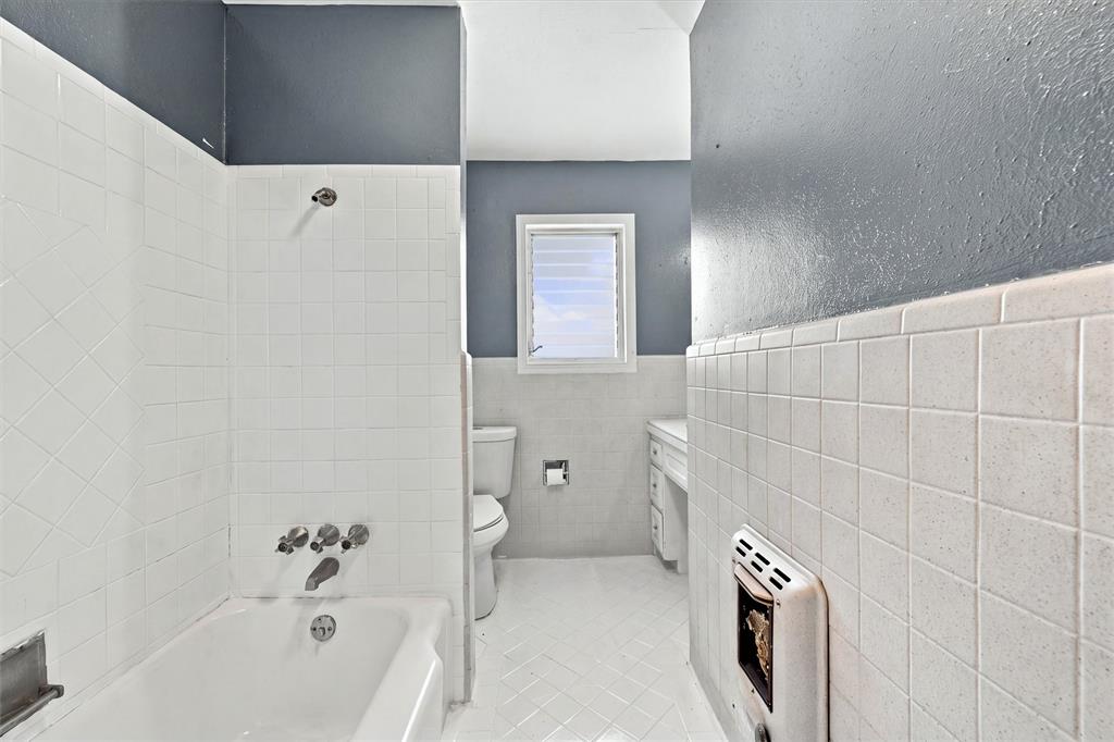 Bathroom featuring a white porcelain tub with integrated shower fixture, white ceramic wall tile, white tiled flooring, and a window with louvered glass panes