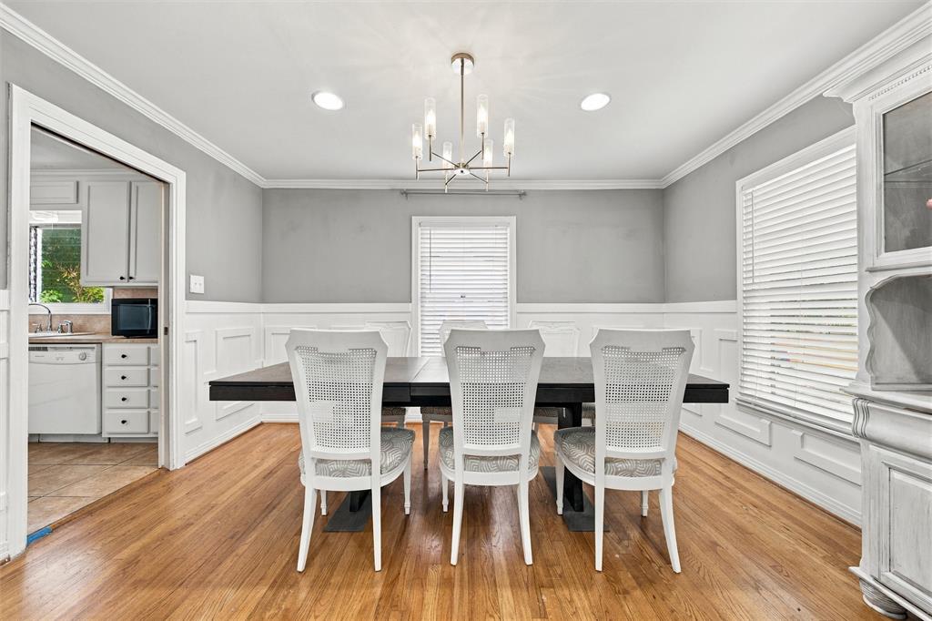 Dining room featuring wood-finish flooring, white wainscoting, crown molding, and a central multi-arm light fixture
