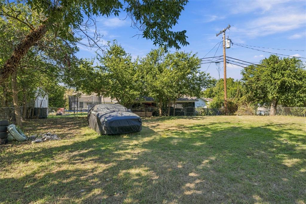 Open grass lot featuring mature trees and chain-link fencing
