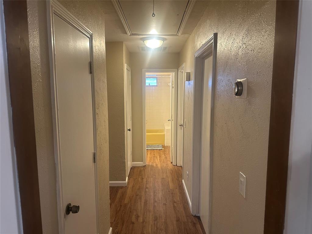 Interior hallway featuring wood-finish flooring, textured wall surfaces, multiple closet doors with round hardware, and a ceiling-mounted light fixture