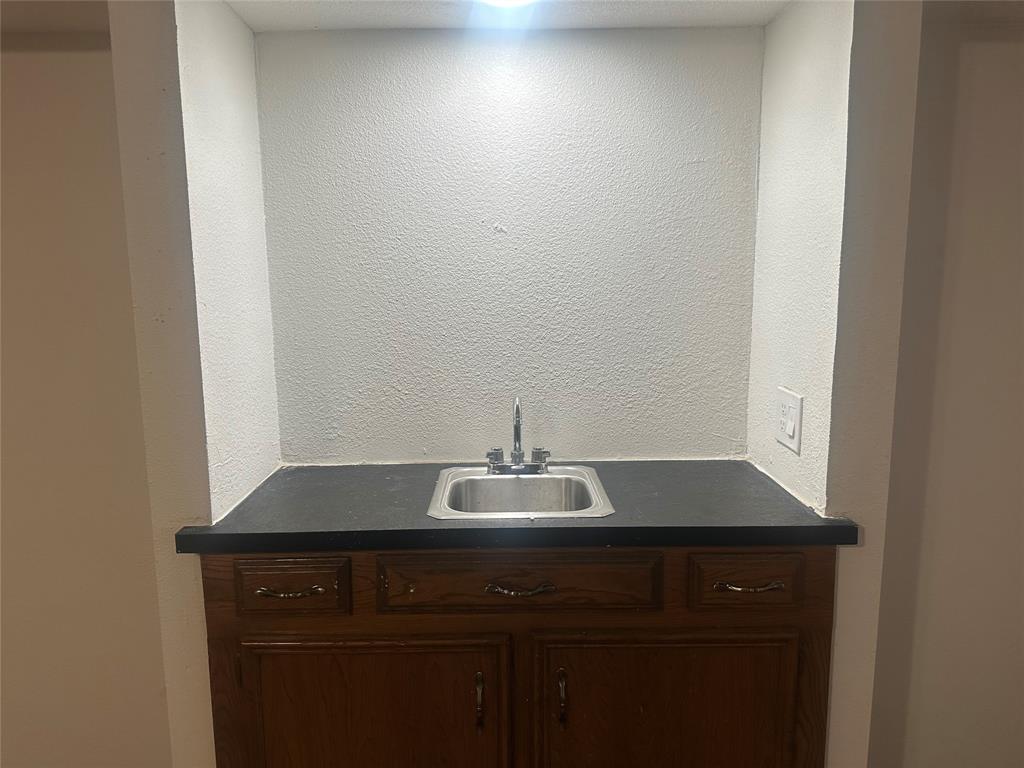 Built-in wet bar featuring a recessed alcove, dark countertop, stainless steel drop-in sink, and wood-finish cabinetry