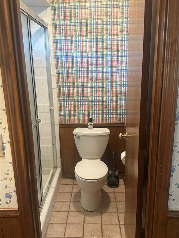 Shower enclosure with metal-frame door, ceramic floor tile, wood-paneled walls, and wallpaper finish