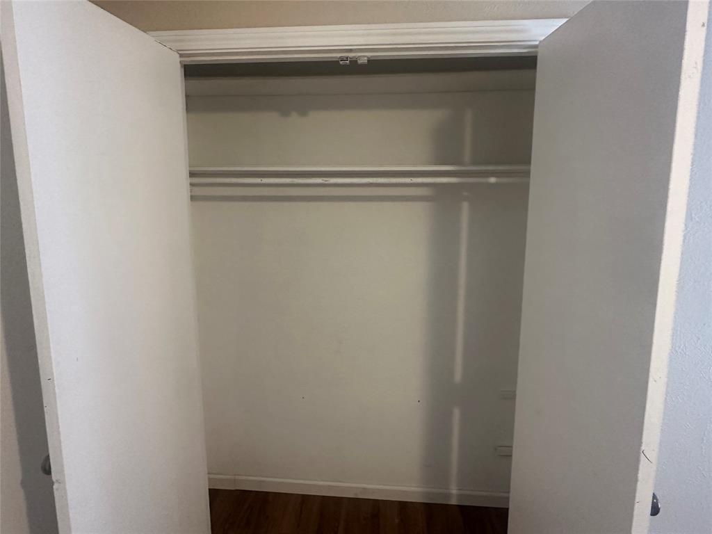 Double-door closet featuring a built-in horizontal clothing rod, overhead shelving, and wood-finish flooring