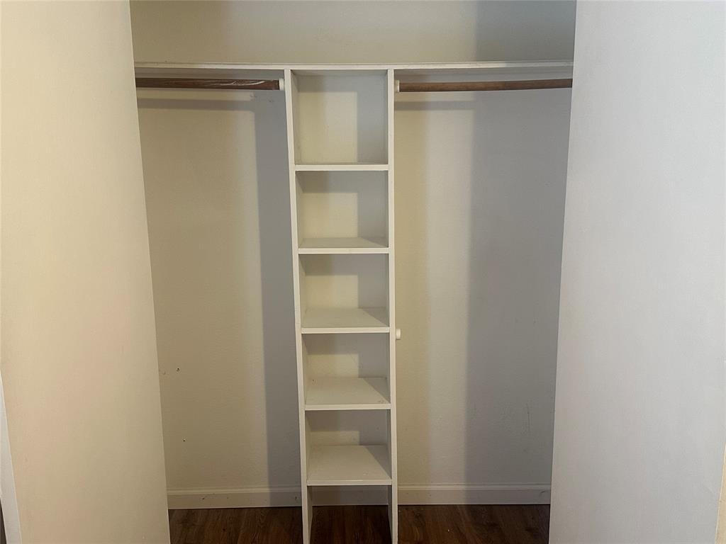 Closet featuring built-in vertical shelving, dual clothing rods, and wood-finish flooring