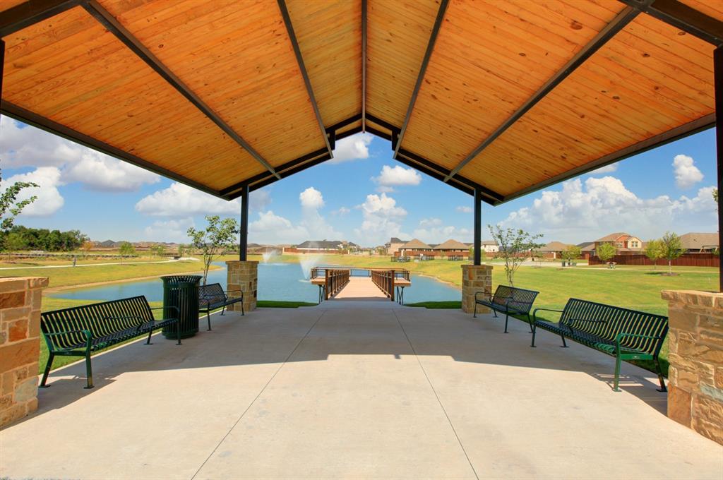 Covered outdoor pavilion featuring a timber-planked gable roof, structural steel supports, and stone-clad masonry pillars, opening to a concrete walkway and waterfront pier