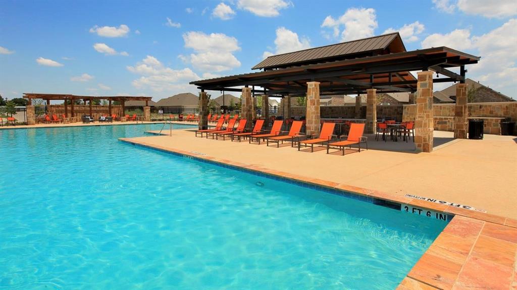 Swimming pool with a textured concrete deck, covered pavilion featuring stone columns, and metal roofing